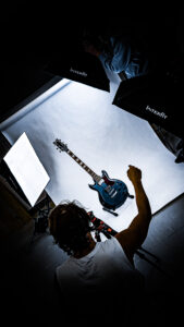 Digi Design Group photo of photographer in studio directing lighting equipment to take product photo of blue ibanez guitar