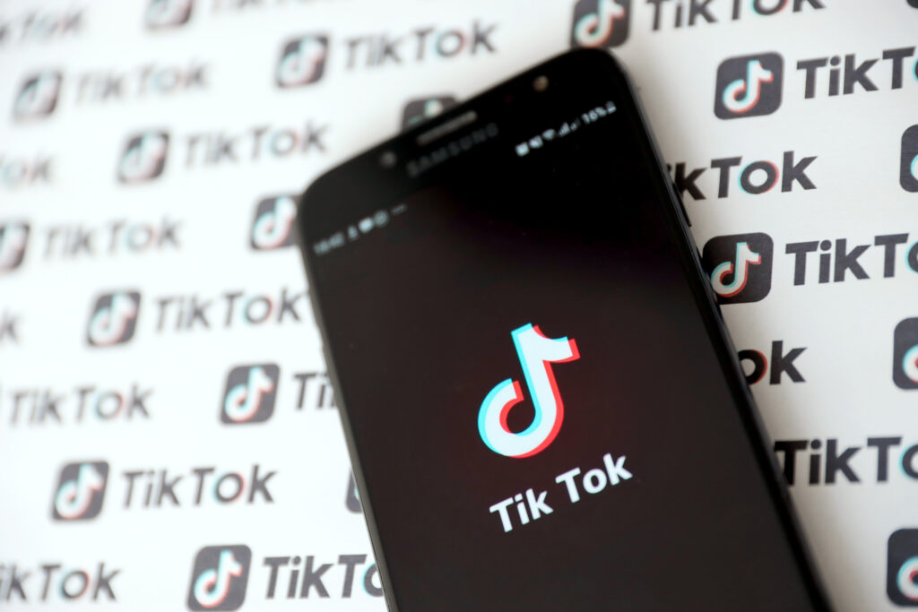 Adobe Stock Photo of Tik Tok smartphone app on screen and Many TikTok logo printed on paper. Tiktok or Douyin is a famous Chinese short-form video hosting service owned by ByteDance Ltd